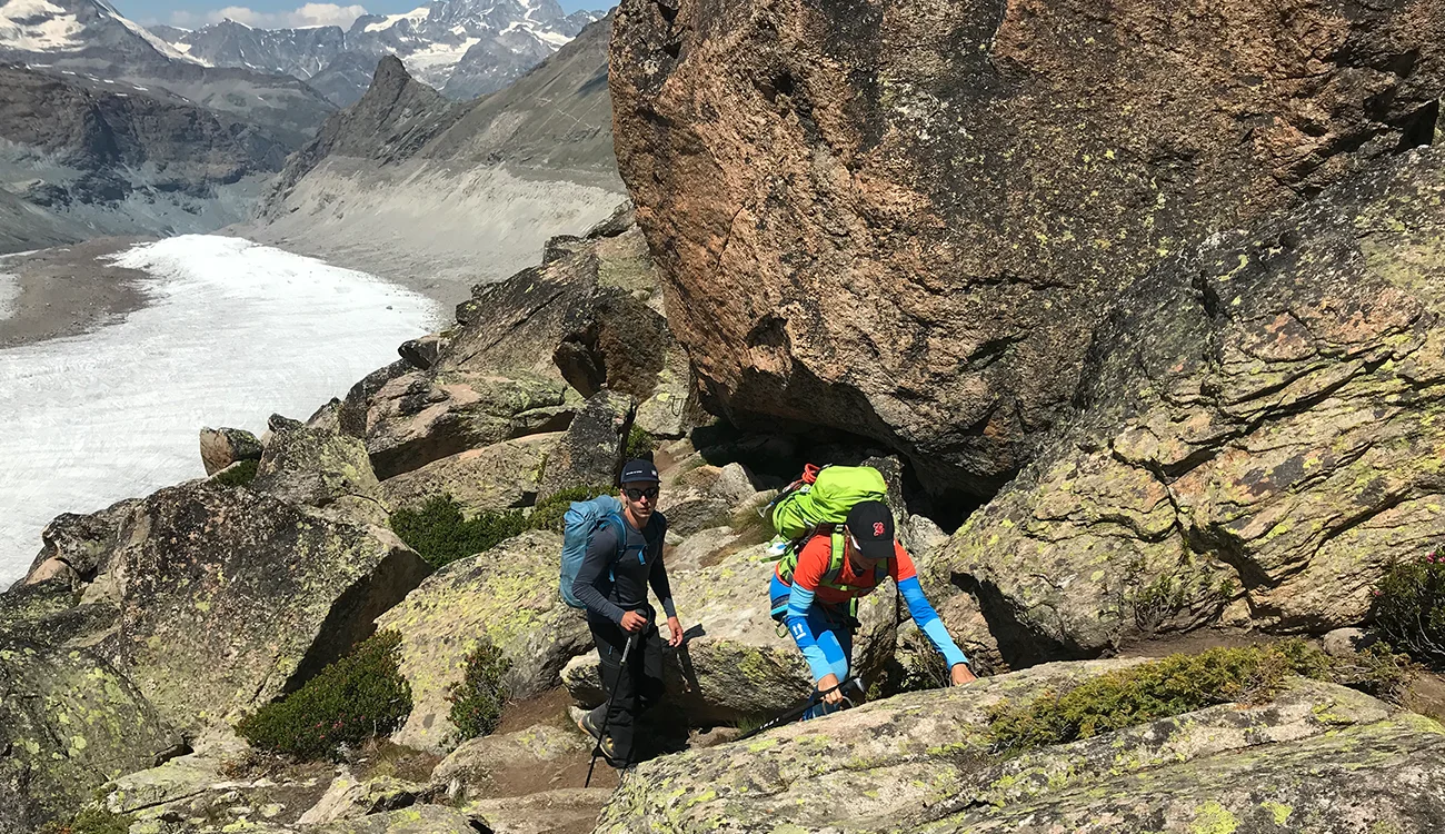 Two hikers making their way through rocky alpine terrain above a glacier during a heli-hiking safari in the Alps