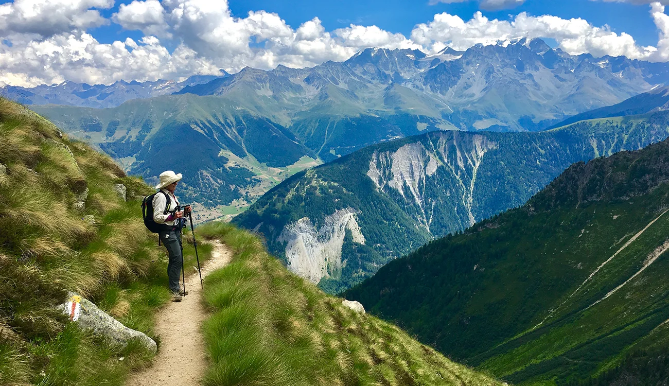 A hiker pauses on a high Alpine trail to take in a vast mountain panorama on a clear summer day