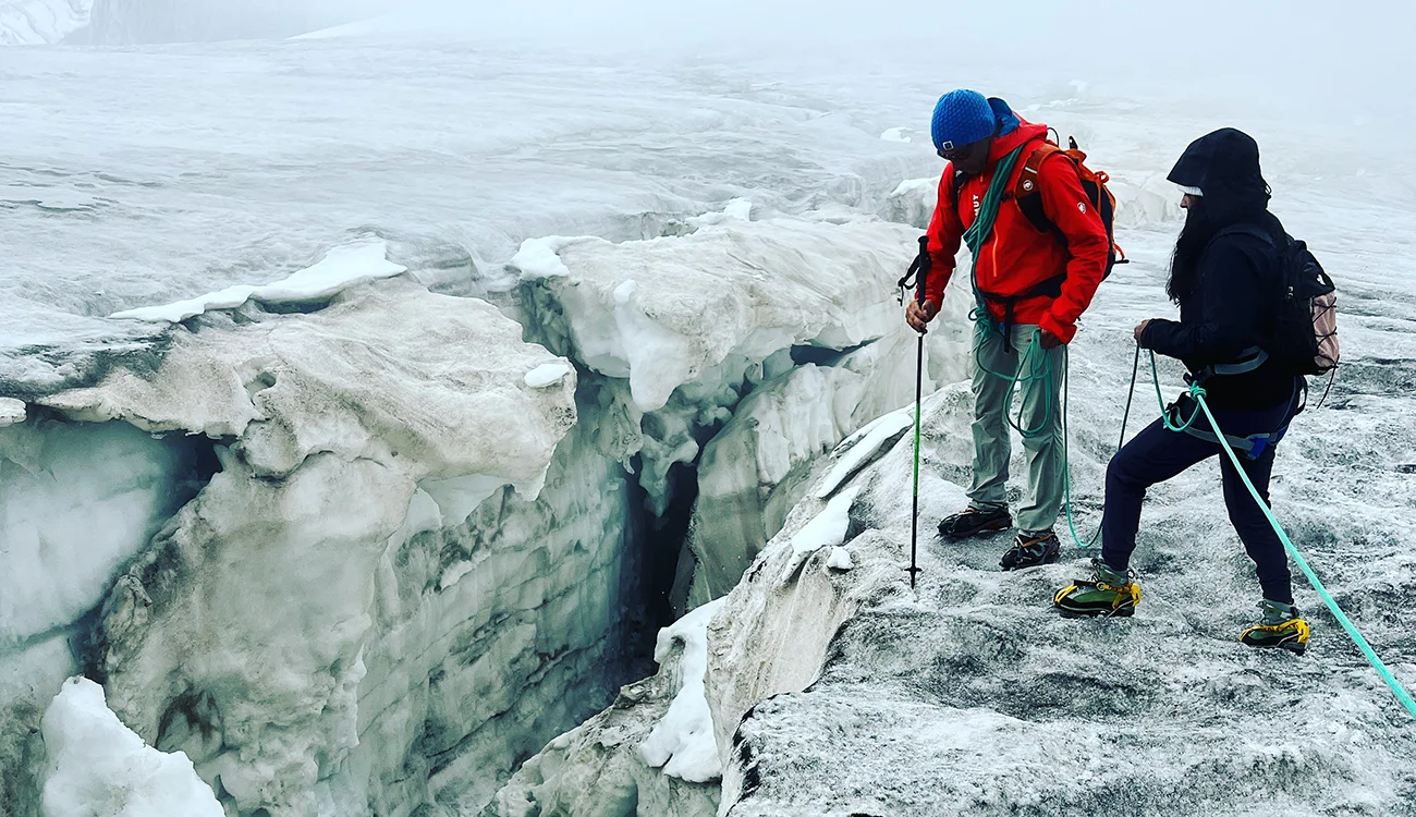 A mountain guide and client peer into a deep glacial crevasse on a high-altitude Alpine crossing