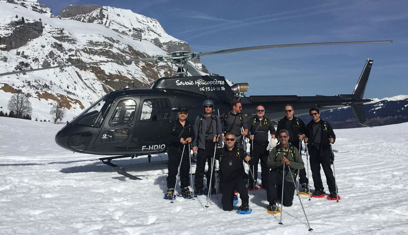 A group of friends standing in front of a helicopter on a snowy alpine landscape during a SwisSkiSafari heli-hiking safari