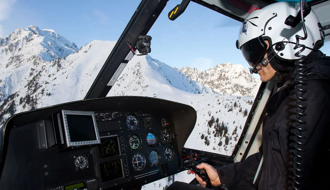 A helicopter pilot in the cockpit flying over the Alps during a SwisSkiSafari heli-hiking safari