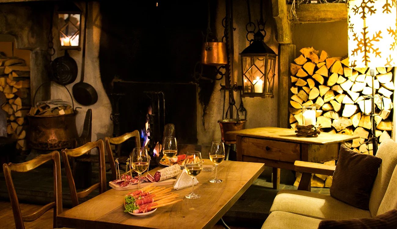 historic-alpine-interior-aperitivo-swisskisafari-beyond-the-trail-1300x750 A warmly lit ancient room with rustic character set for pre-dinner drinks in an Alpine bar