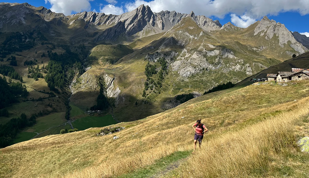 A hiker walks through an Alpine pasture on a gentle mountain approach trail surrounded by peaks
