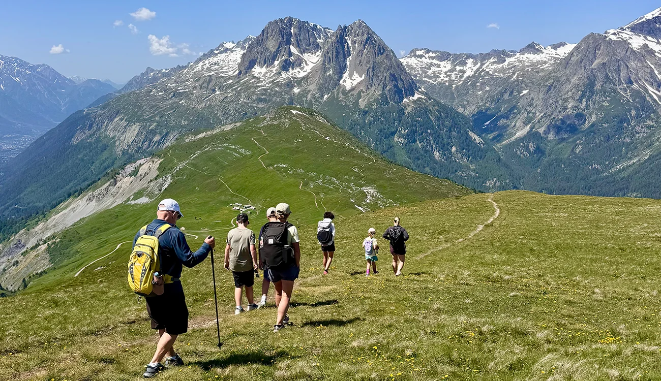 Small group hiking an alpine trail with distant mountains, Alps