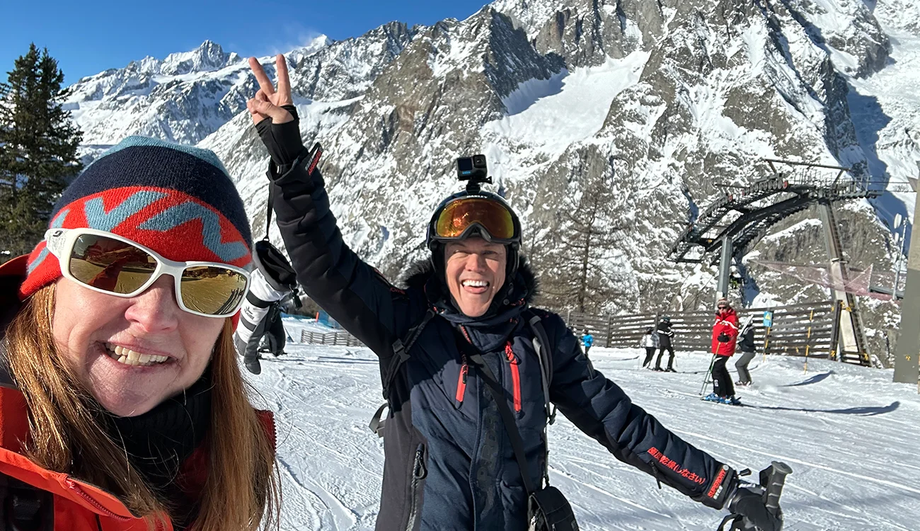 ski-safari-alps-skiers-celebrating Ski guide and client giving a peace sign on a sunny ski slope with snow-capped mountains in the background