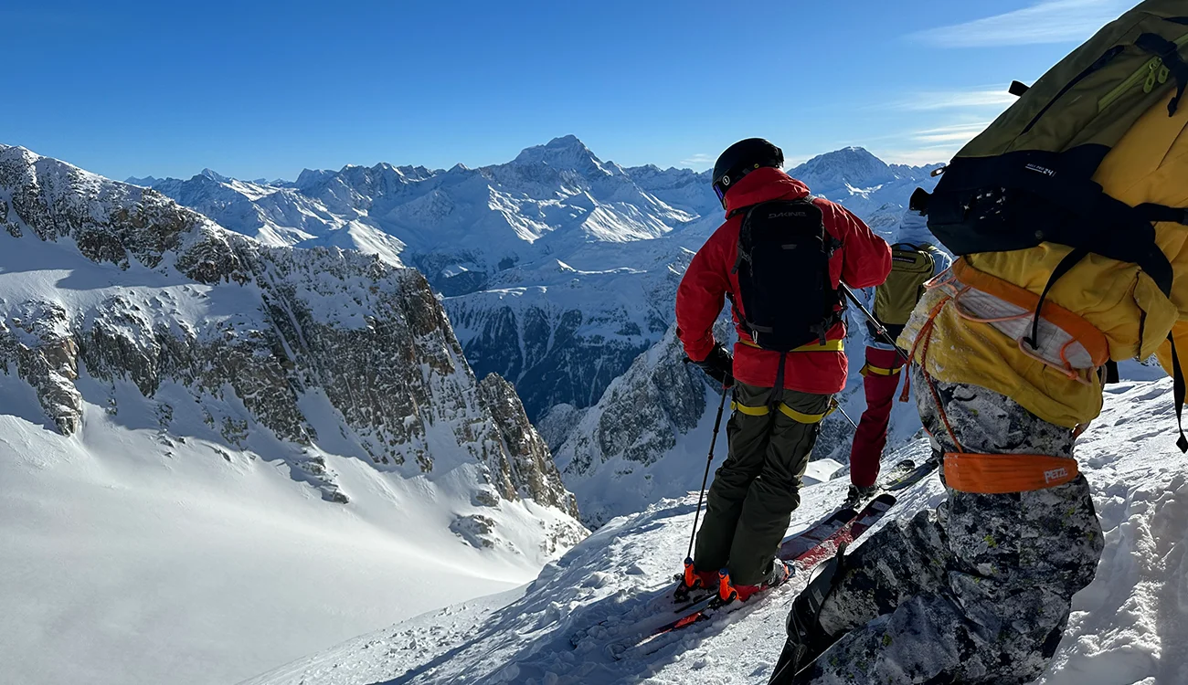 skier-and-snowboarder-ready-to-descend-alps Skier and snowboarder standing on a mountainside in the Alps ready to descend during a guided safari